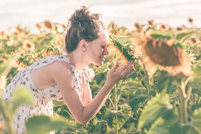 Side view of woman smelling flower on field