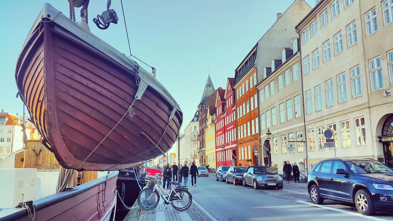 building exterior, architecture, transportation, built structure, land vehicle, car, mode of transport, street, city, clear sky, road, city life, incidental people, day, the way forward, building, city street, sunlight, men