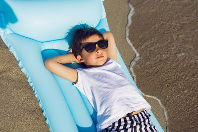 Child boy in sunglasses, a white t-shirt lies on an inflatable mattress on the seashore