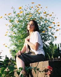 Young woman sitting against plants and trees against sky