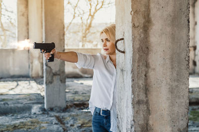 Woman holding gun while standing amidst columns