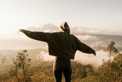 Rear view of woman with arms outstretched while standing on mountain