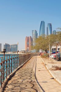 Footpath leading towards buildings against clear sky