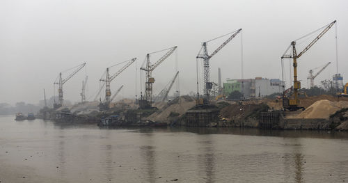 Cranes at harbor against sky