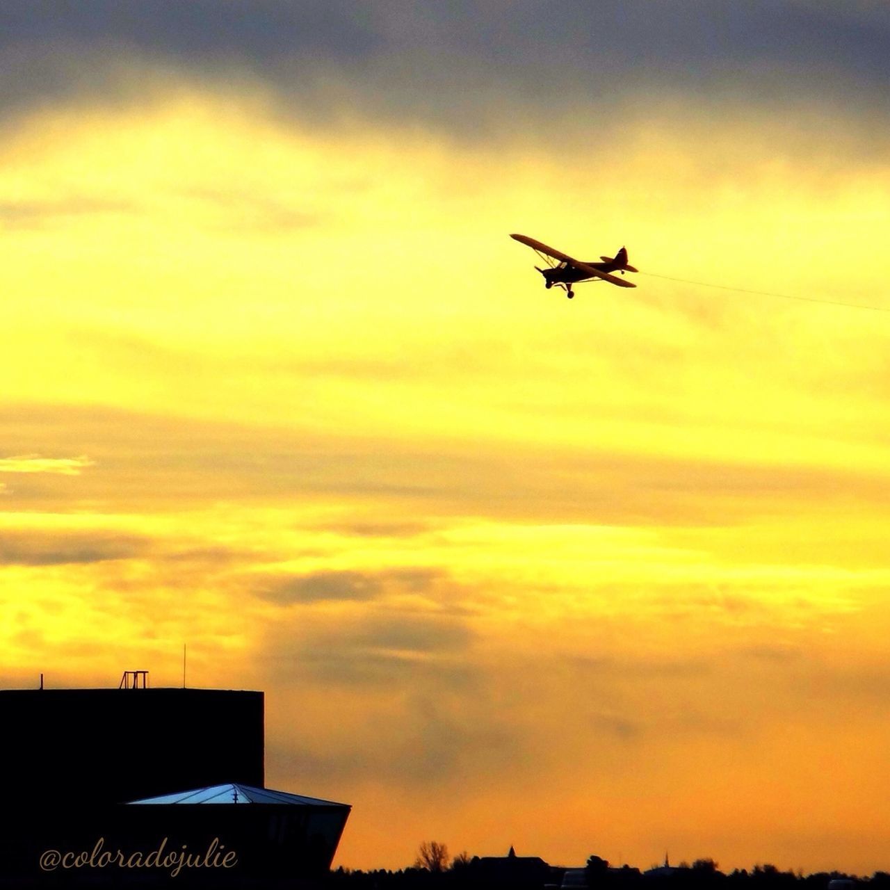 sunset, airplane, flying, air vehicle, sky, orange color, cloud - sky, silhouette, mode of transport, transportation, mid-air, building exterior, architecture, built structure, dramatic sky, low angle view, cloud, cloudy, beauty in nature, nature