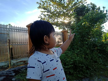 Girl looking away while standing by plants against sky