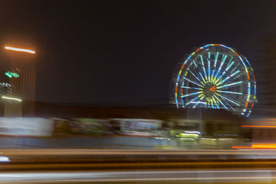 Blurred motion of illuminated ferris wheel in city at night