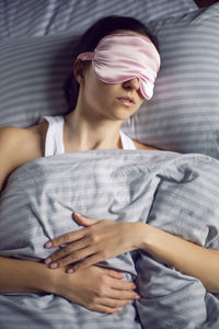 Woman in a pink eye mask lies under a blanket in a bed and suffers from insomnia 