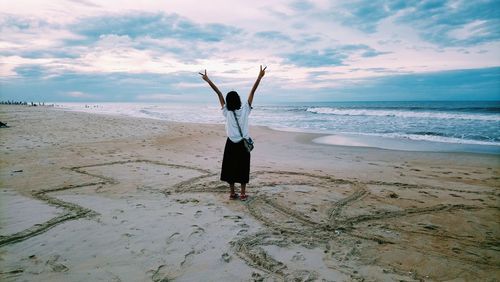 Rear view of woman standing at beach against sky