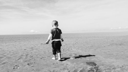 Rear view of boy standing on beach against sky