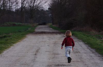 Rear view of girl running on footpath by road