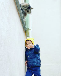 Portrait of boy pointing while standing by white wall