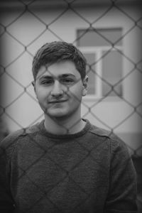 Portrait of a smiling young man looking through chainlink fence