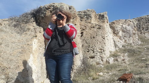Woman photographing through camera against rock