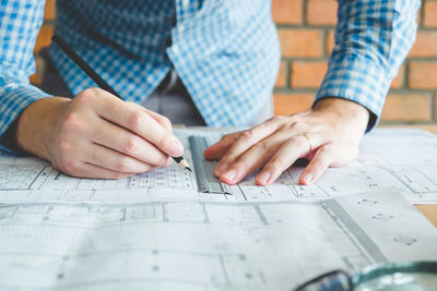 Midsection of man drawing on blueprint at desk