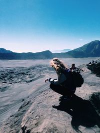 Full length side view of woman crouching against volcanic landscape