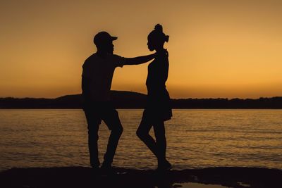 Silhouette couple standing against sea during sunset