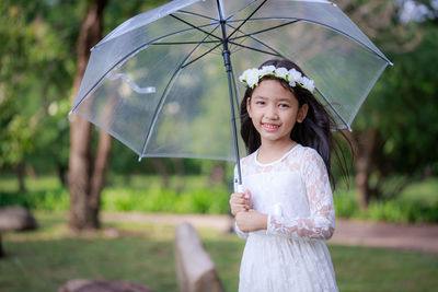 Cute girl holding umbrella while standing in rain during rainy season