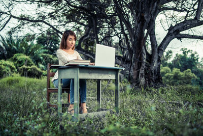 Woman using laptop on table amidst field