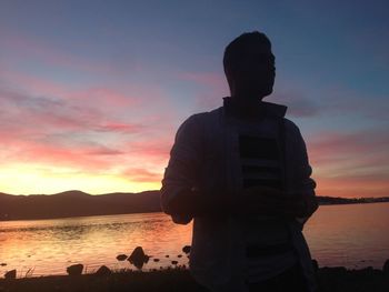 Rear view of silhouette man standing by lake against sky during sunset