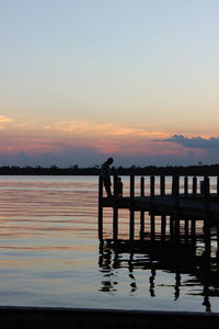 Silhouette man standing by lake against sky during sunset