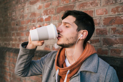 Portrait of young man drinking against wall