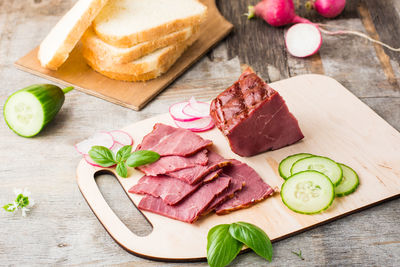 Fresh sliced marbled beef pastrami, cucumber, radish and basil on a cutting board