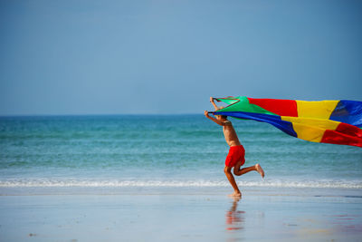 Rear view of woman holding umbrella at beach against clear sky