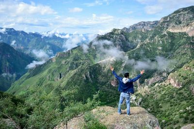 Full length of man climbing on mountain against cloudy sky