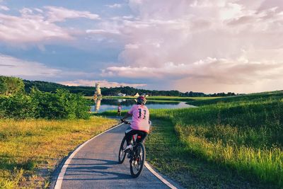 Man riding bicycle on road amidst field against sky