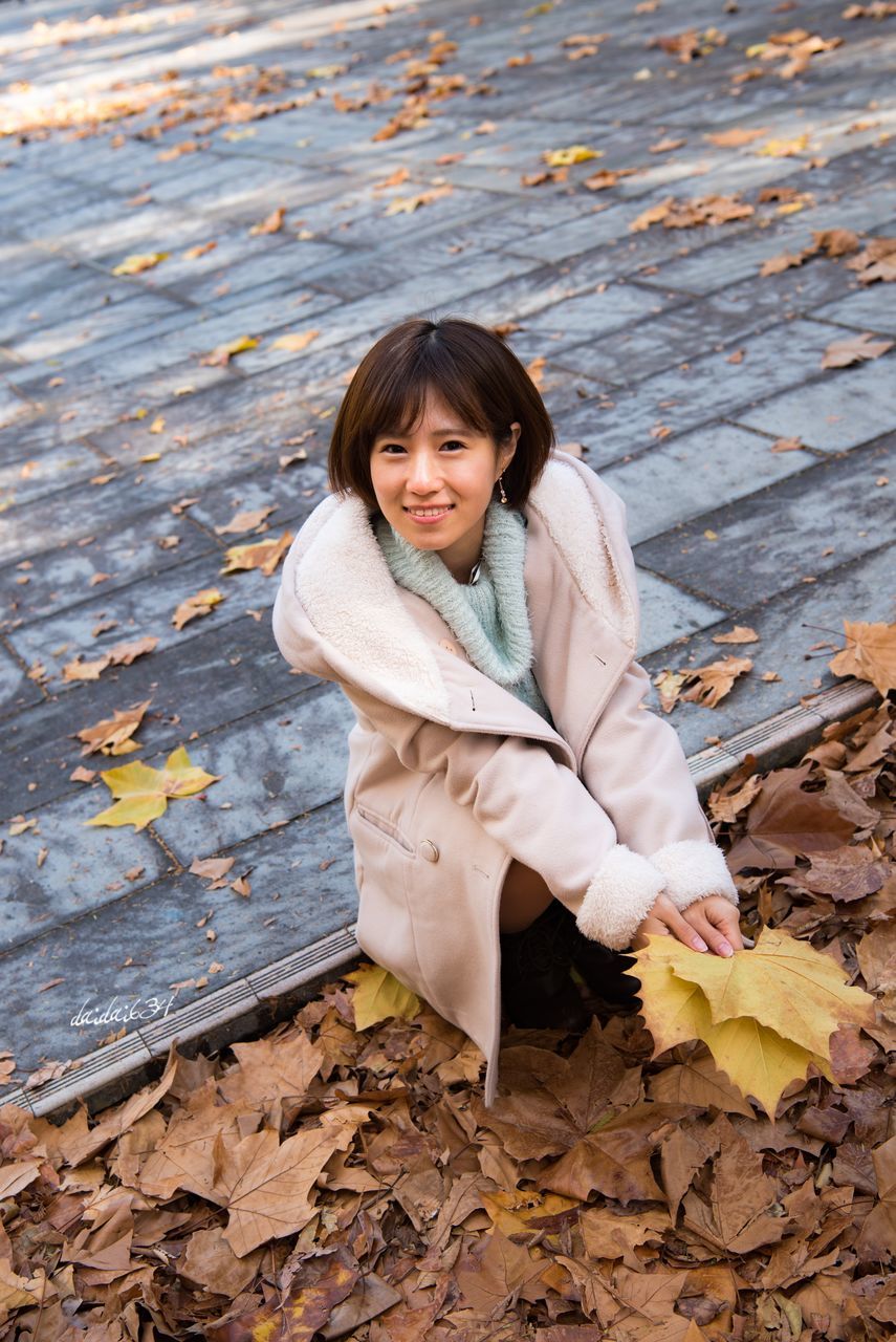 autumn, leaf, real people, one person, looking at camera, change, young women, young adult, smiling, outdoors, portrait, lifestyles, long hair, leisure activity, day, full length, front view, nature, standing, happiness, beautiful woman, beauty in nature, warm clothing, people