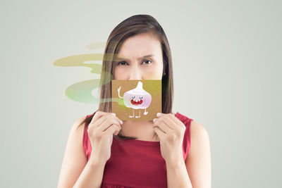 Portrait of woman holding placard with garlic emitting smell against gray background