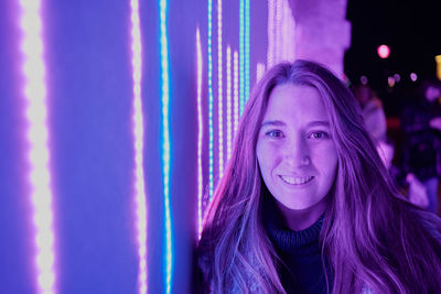 Portrait of beautiful young woman against illuminated wall at night