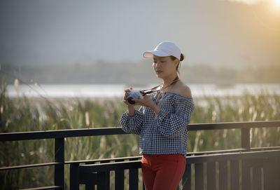 Woman photographing with camera while standing against railing