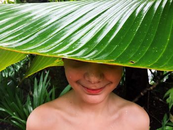 Close-up of smiling teenage boy hiding behind leaf