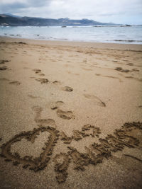 Heart shape on sand at beach against sky