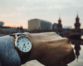 Cropped image of hand wearing wristwatch with oberbaumbruecke in background