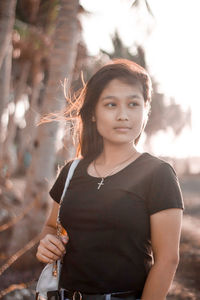 Portrait of young woman standing against trees