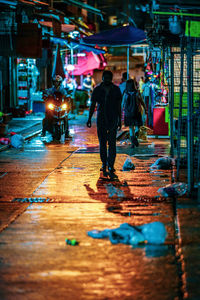 Rear view of people walking on illuminated street at night