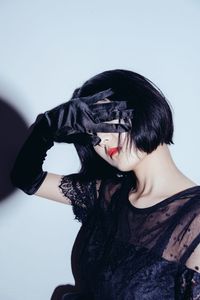 Portrait of young woman shielding eyes against black background