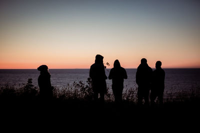 Silhouette people standing by sea against sky during sunset