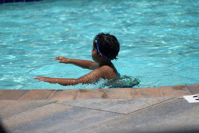 Rear view of shirtless boy swimming in pool