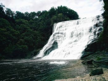 Scenic view of waterfall in forest against sky