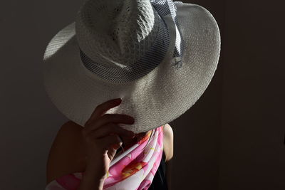 Close-up of woman holding hat against black background