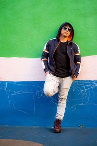 Handsome young man posing and wearing sunglasses witt a colorful wall as background.