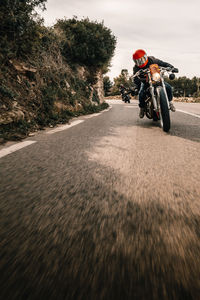 Unrecognizable bikers riding motorcycles on curve of narrow asphalt road going through mountainous terrain