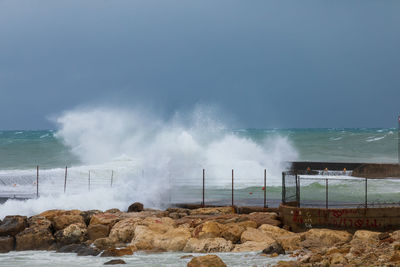 Waves splashing on rocks at shore against sky