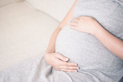 Midsection of pregnant woman sitting on sofa at home