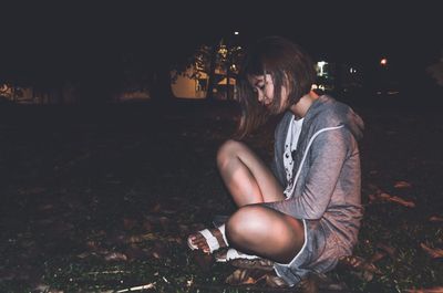 Full length of young woman sitting on field at night