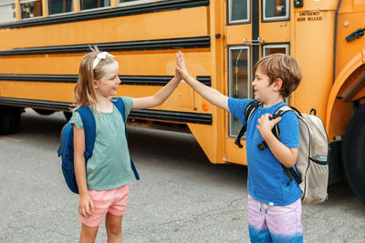 Children boy and girl kids students give high five by yellow school bus. education  back to school